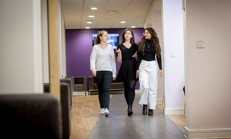 3 female students walking down a corridor chatting 