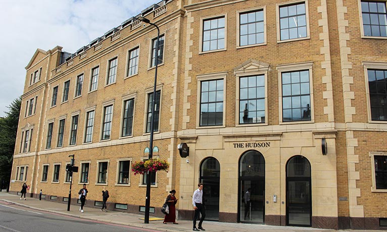 Two people walking in front of the Hudson building in London