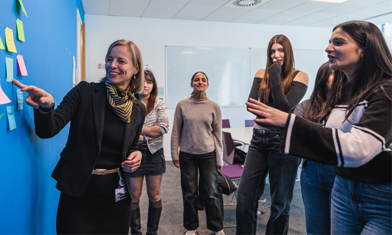 A tutor with students using a post-it note wall in the marketing hub