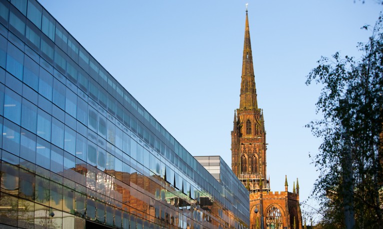 Long side of building on a sunny day, with a church in the background