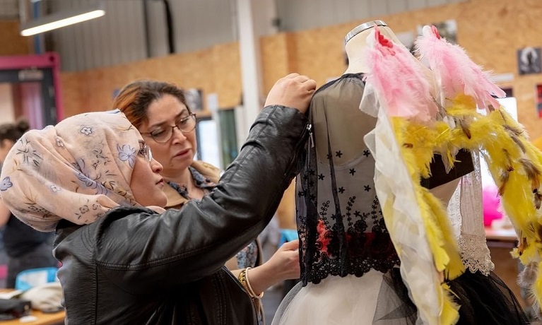 Two women attaching material to an outfit on a mannequin