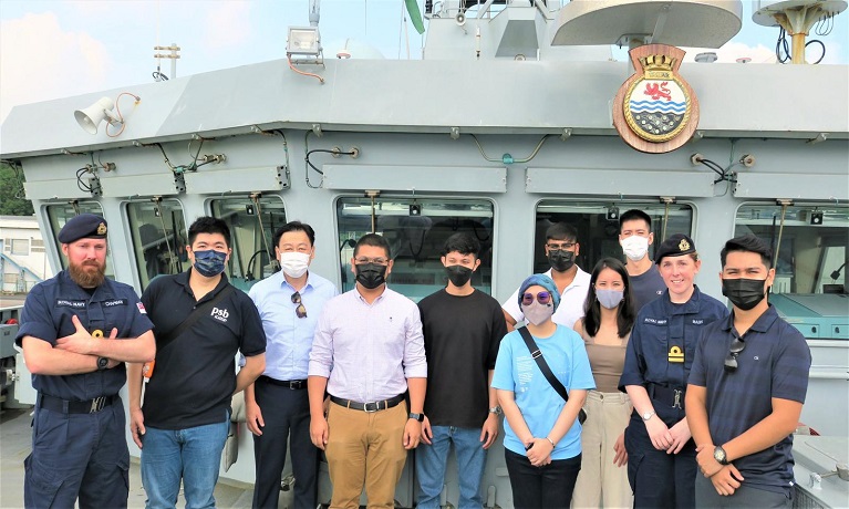 A group of students standing on the deck of a ship with members of the crew