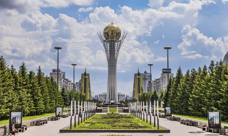 An image of the city of Astana showing a tree-lined open area with a tower topped by a gold orb at the central point