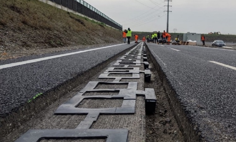 An image of a road with panels laid out in a long hole in the surface of the carriageway while people in hi-vis clothes are in the background