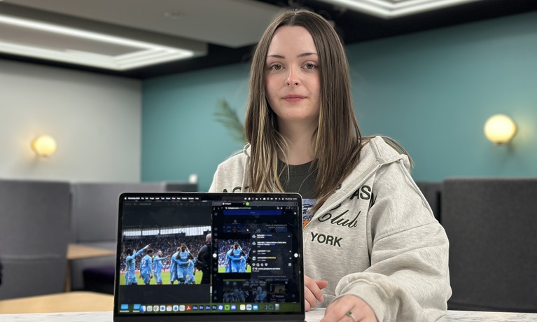 Jess Pearson in a grey jumper with photos she has taken of Coventry City FC on a laptop