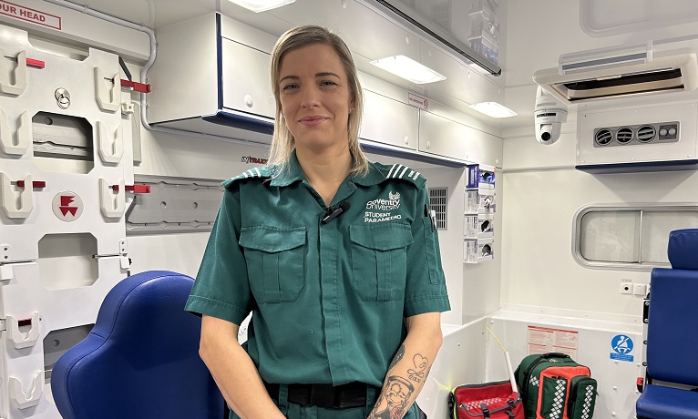 Gemma White in her green paramedic uniform inside Coventry University's replica ambulance.