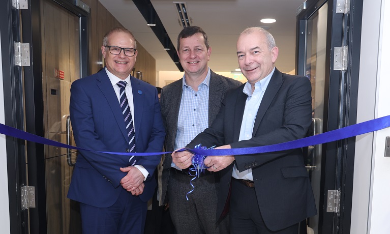 Three men cutting a ribbon across a doorway