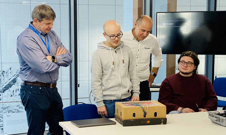 A student stood up next to his device sat on a table in front of him speaking to a Coventry University Wrocław staff member on his right and a Balluff representative on his left