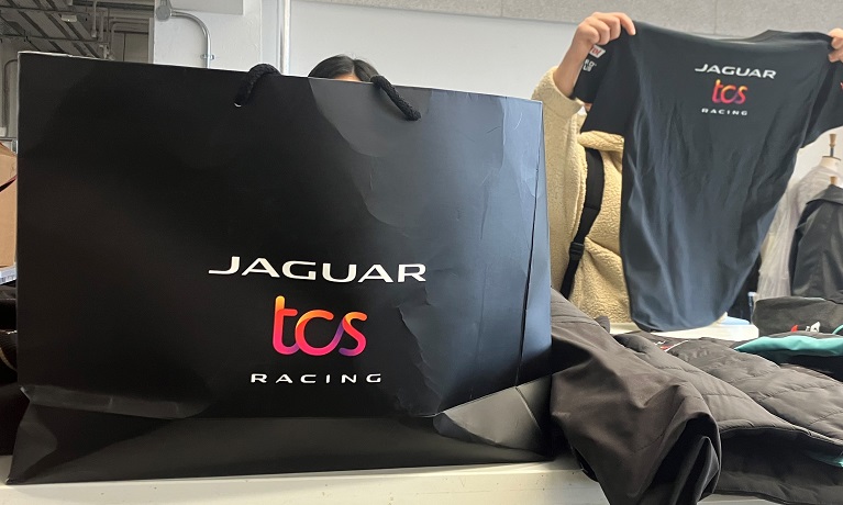 A Jaguar TSC Racing t-shirt being held up by a Coventry University student with a black Jaguar bag seen in the foreground