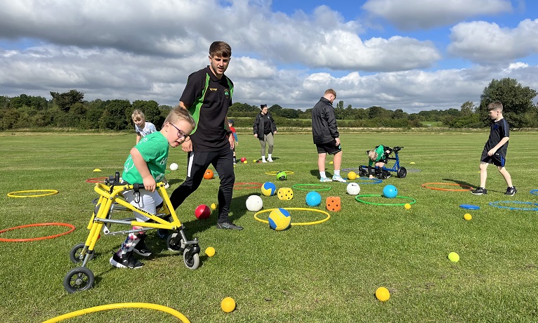 Children with Cerebral Palsy playing football with balls and hoops on a football pitch with a team of coaches helping them.