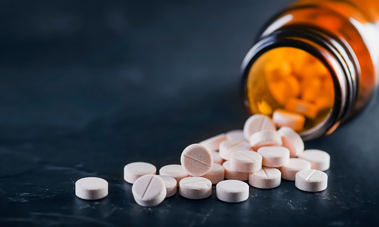 A bottle of tablets on its side with the lid off and tablets pouring out of it