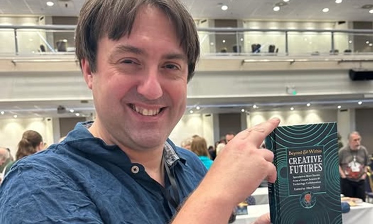 Dr Allen Stroud smiling at the camera while holding a copy of the book Creative Futures