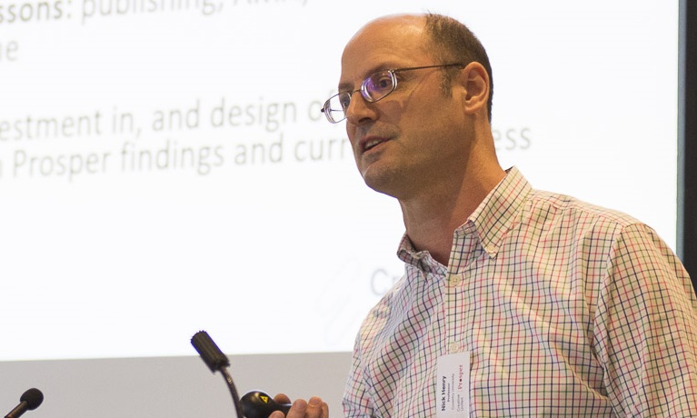 Nick Henry (white male with glasses) speaking at a conference