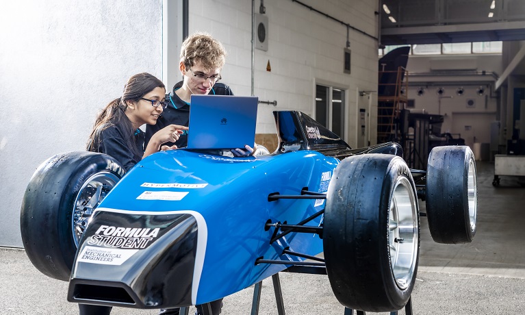 Two Mechanical Engineering students using a laptop to collect data from a blue autonomous sports car 