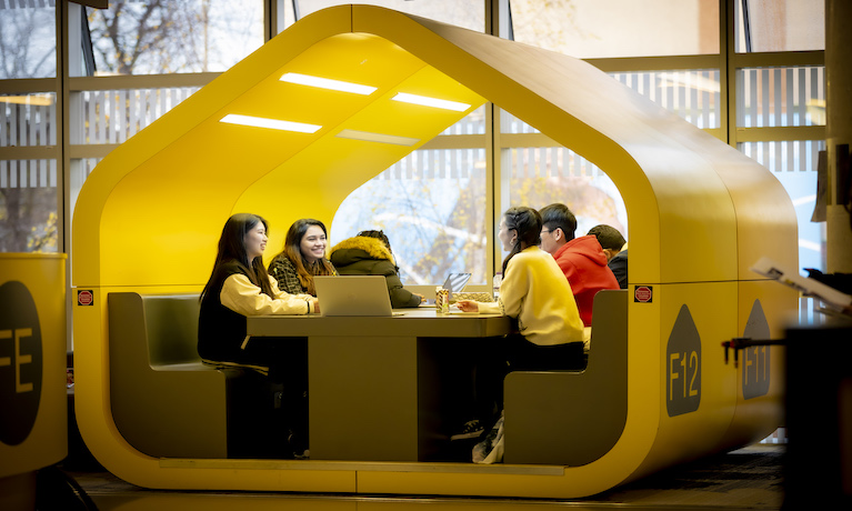 A group of students sitting and working together in a yellow pod