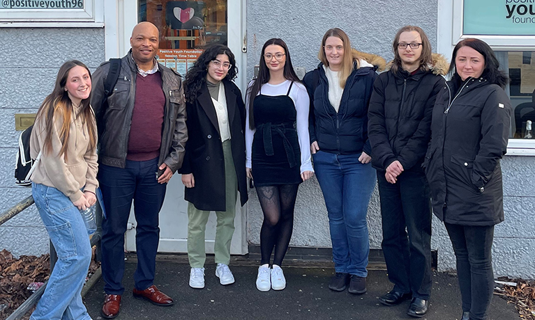 A group of seven students standing outside of the entrance to a community centre