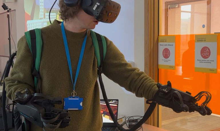 A student wears a virtual reality helmet and glove, reaching out to one side.