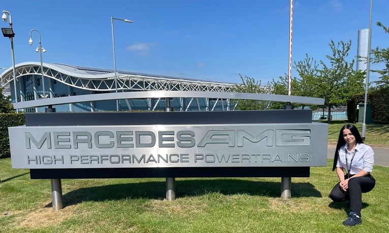 Ines kneeling down beside the Mercedes company sign