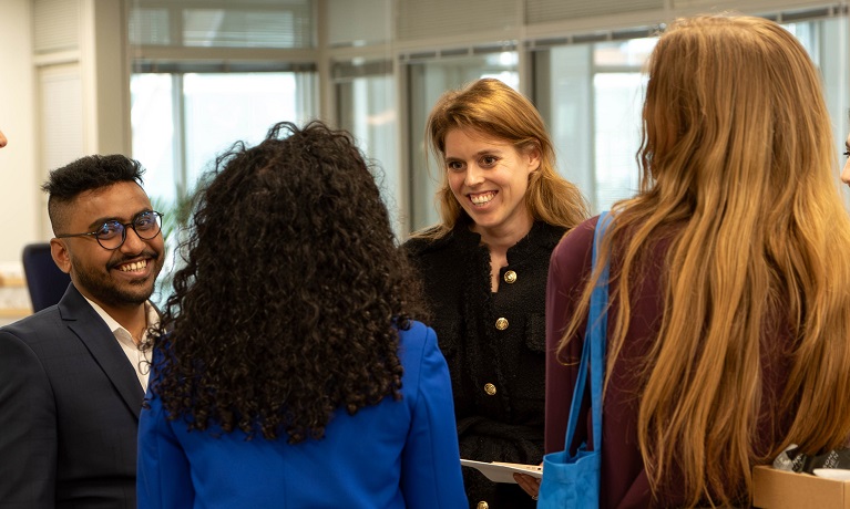 Mahbub Shuhag wearing a dark suit and glasses speaking with HRH Princess Beatrice along with two women with their backs to the camera