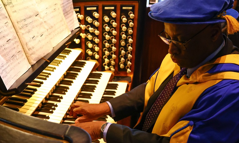Wayne Marshall in his Coventry University graduation gown and cap playing the organ at Coventry Cathedral