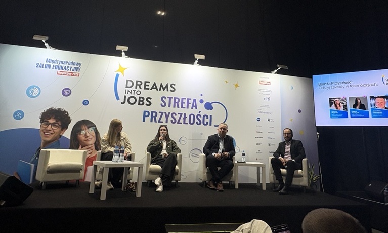 Four people sat on a stage with a 'Dreams into Jobs' backdrop and one of them is speaking into a microphone