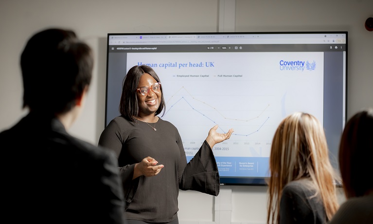 A woman delivering a business presentation on a screen in from of students