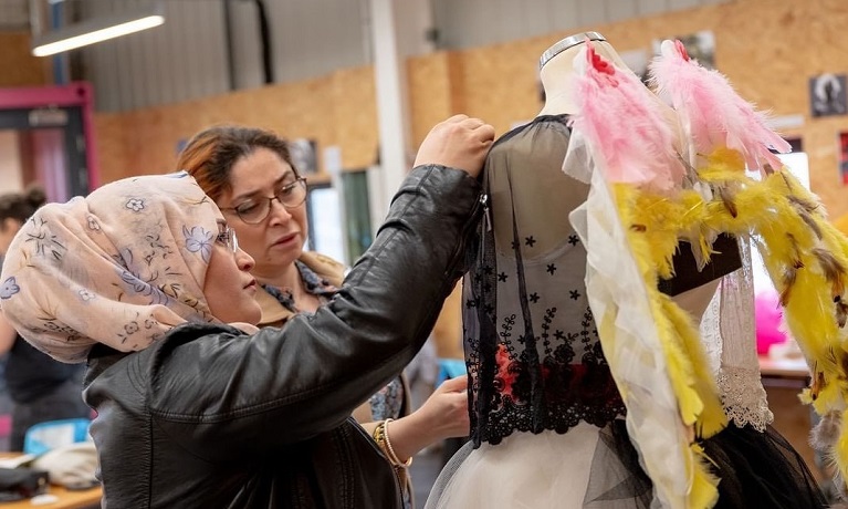 Two women attaching material to an outfit on a mannequin 