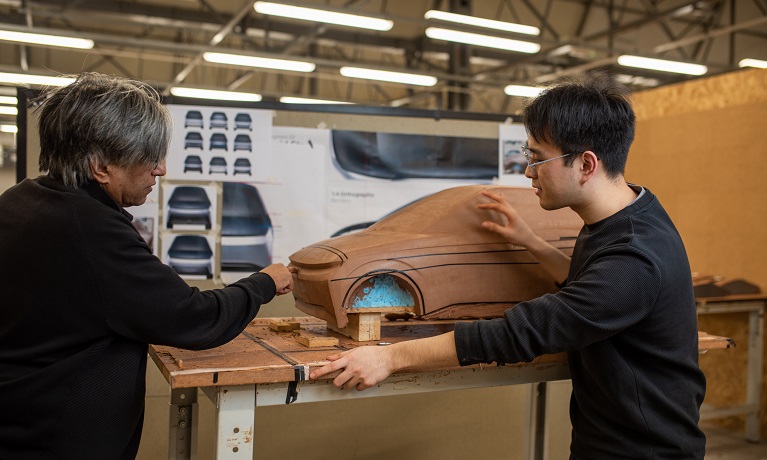 A student and a staff member looking at a clay model of a car n a table at about waist height