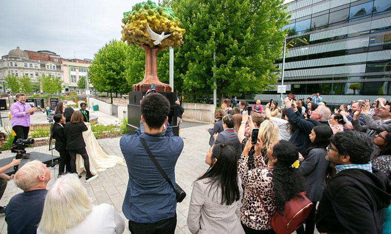 A crowd of people looking at the Tree of Peace statue