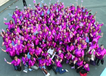 Over 100 people in matching pink tops look up at the camera