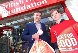Two people outside BHF shop, one holding a bag of donations and the other wearing a BHF tshirt
