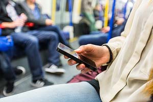 Someone sat down using a mobile phone on a tube