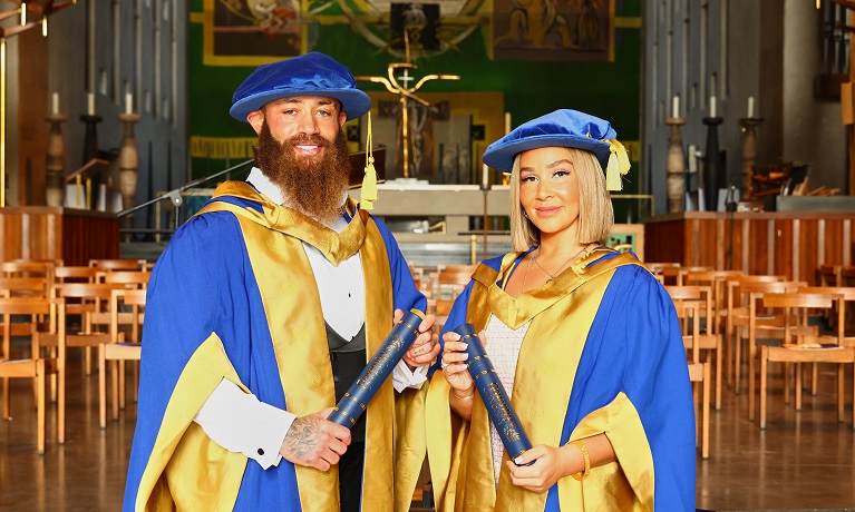 Ashley and Safiyya holding their Honorary Doctorates in Coventry Cathedral