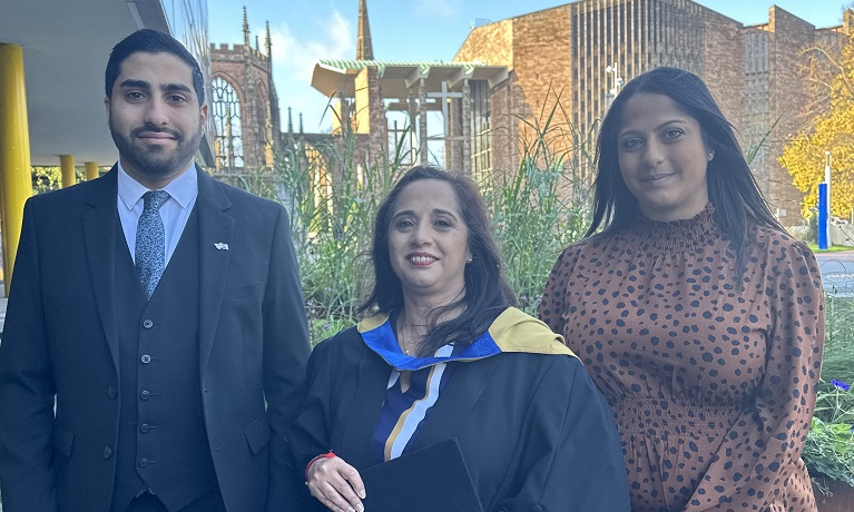 Manvinder Dukhi wearing her graduation gown stood between her son Harjinder and her daughter Baljinder with Coventry Cathedral in the background