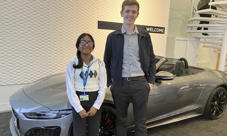 A female and male student standing in front of a car
