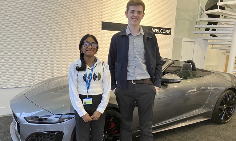 A female and male student standing in front of a car