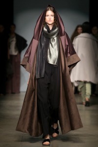 Model on catwalk wearing winnig designs: a grey top, black trousers and brown hooded coat