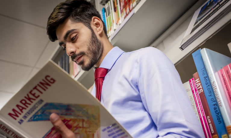Man looking through a book in a library aisle