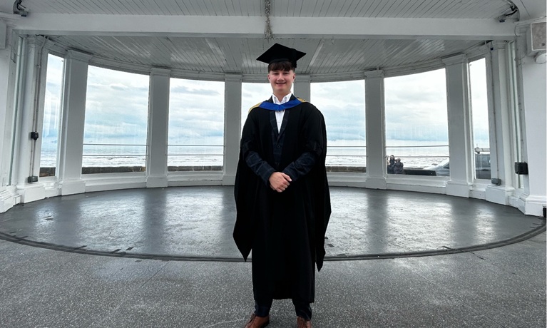 Harvey Williams smiling at the camera wearing his graduation gown and cap