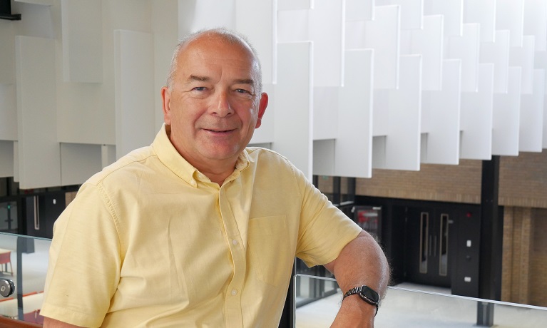 A man in a yellow shirt standing against a balcony