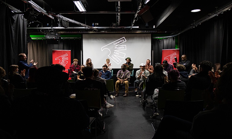 An image of an audience facing a discussion panel on a stage