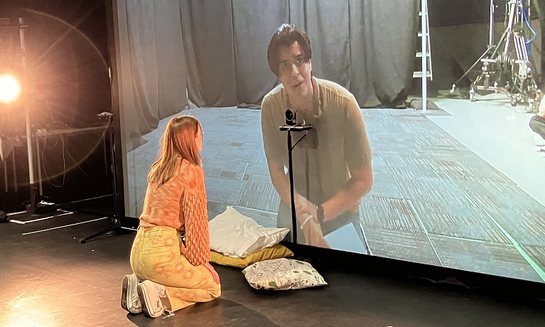 Two student actors interacting through a big screen