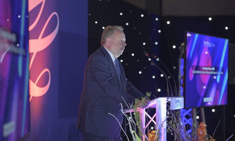 Dr Andy Palmer dressed in a suit stood at a podium on stage at Coventry University's Chancellor's Dinner