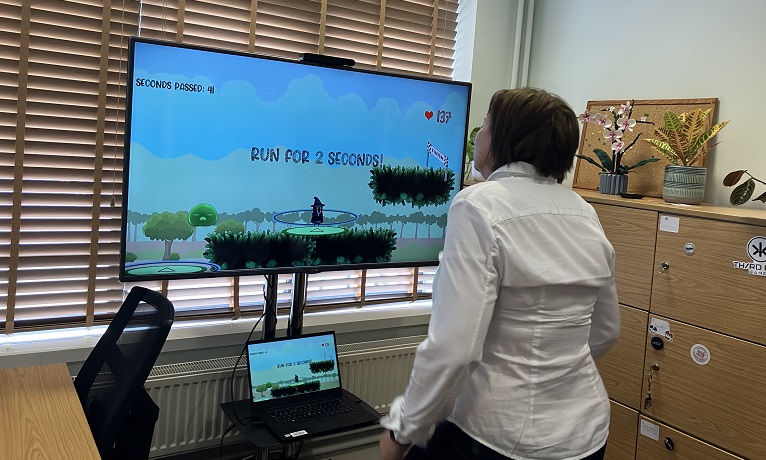 A participant running on the spot in front of a TV screen showing a computer game where the person's heart rate controls the main character