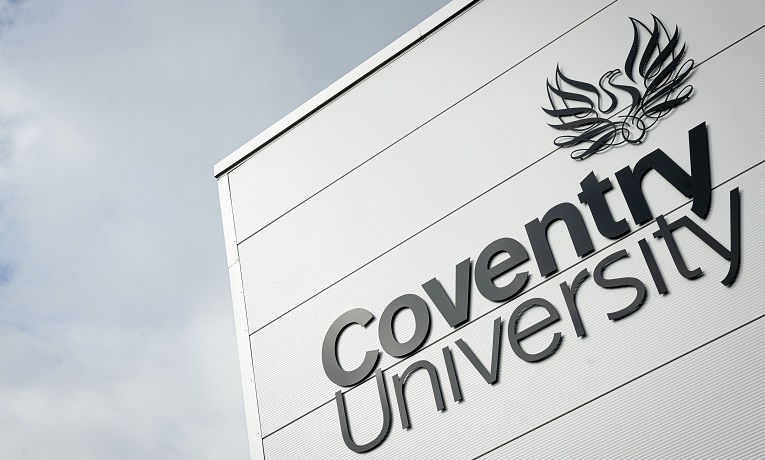 A large Coventry University logo on the side of a white building with clouds in the background