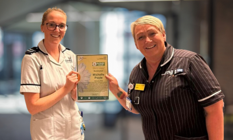 Michelle Poole in her Coventry University student uniform is handed her DAISY Award nomination by a colleague at University Hospital Coventry and Warwickshire