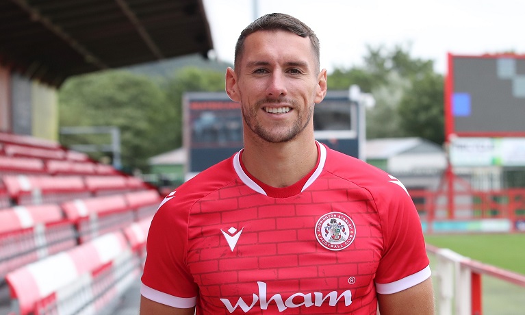 Matt Lowe wearing his Accrington Stanley kit while stood with the one of the stands from the stadium behind him