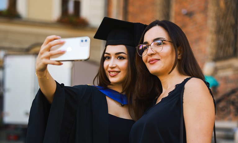 A student wearing her graduation gown and cap takes a selfie on a mobile phone with a loved one at the first ever Coventry University Wrocław graduation ceremony