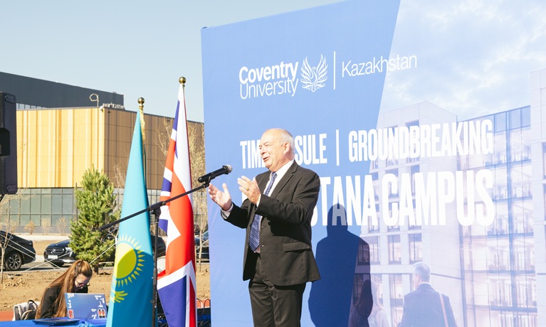 Professor John Latham CBE speaking on stage at groundbreaking event in Astana