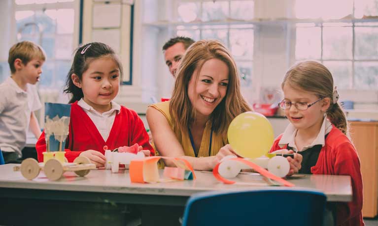 Teacher in classroom with two children with a balloon and materials